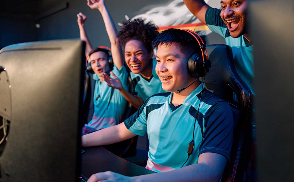 Team of excited cybersports gamers looking at PC screen and celebrating success while participating in esports tournament in gaming club